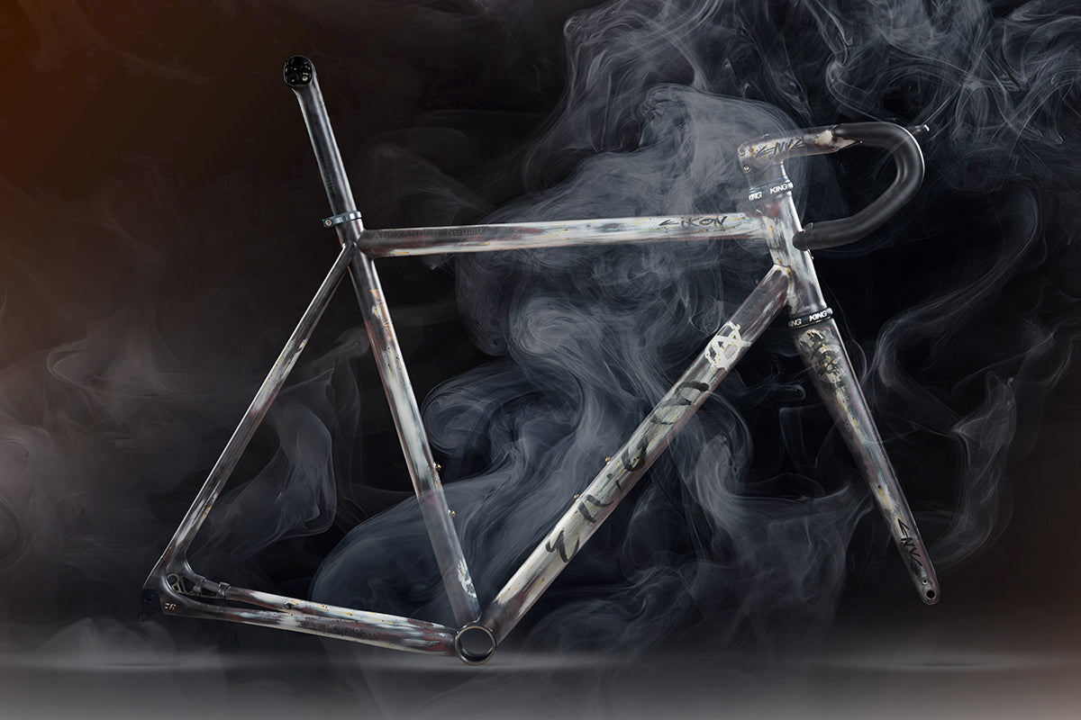 Enigma Eikon titanium bike frame emerging through smoke, showcasing its raw brushed finish and bold, artistic presentation.