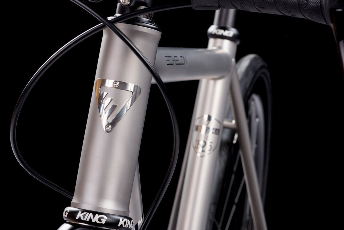 Close-up of an Enigma titanium bike frame highlighting the head tube, head badge and brushed titanium finish.