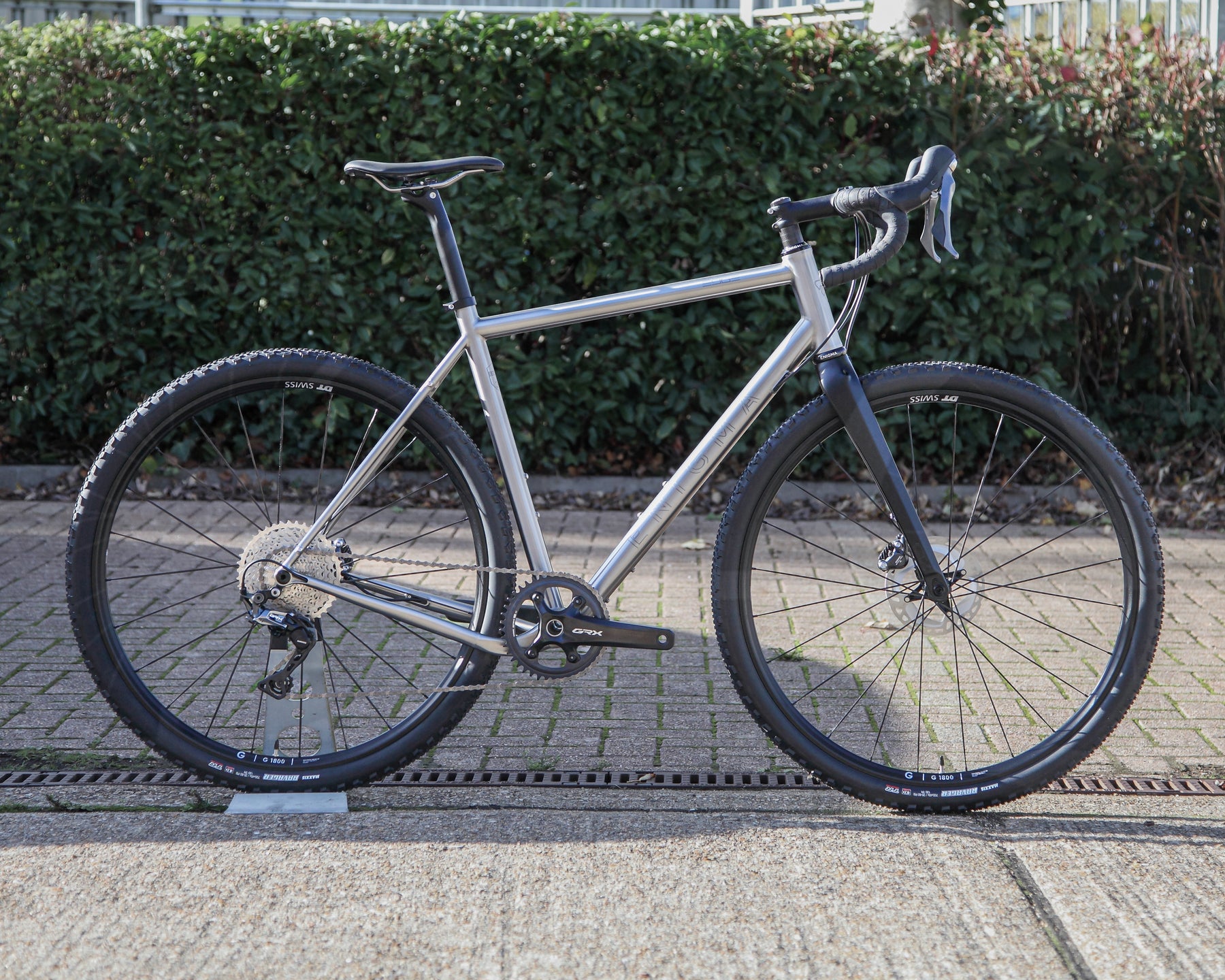 Enigma Edge MK.I 56cm titanium gravel bike, side profile showing brushed titanium frame, Shimano GRX drivetrain, DT Swiss gravel wheels, knobbly tyres and black carbon fork.