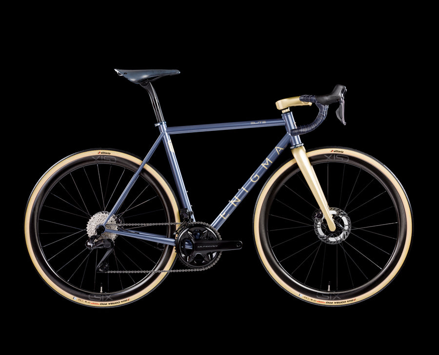 Enigma Elite steel road bike in deep blue and gold with carbon fork, drop handlebars and disc brakes, shown on a black background. Ex showroom steel road bike for sale.
