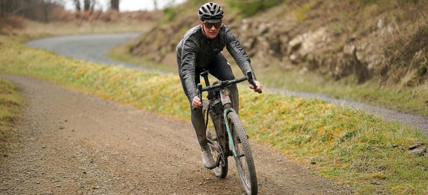 Rider on an Enigma titanium gravel bike riding along a muddy gravel track.