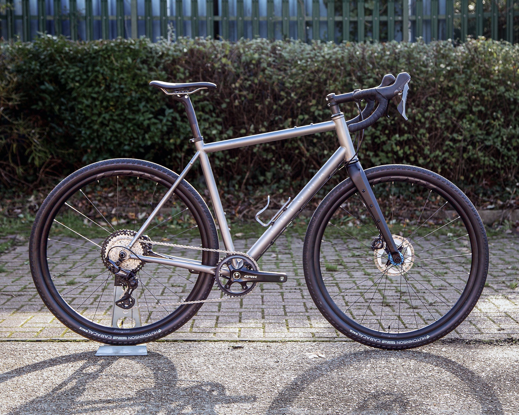Enigma Escape MK.III 56cm titanium gravel bike, side-on view showing satin bead frame with brushed logos, Shimano GRX 1X drivetrain, C-Six ADV carbon fork and Hope RX24 gravel wheels.