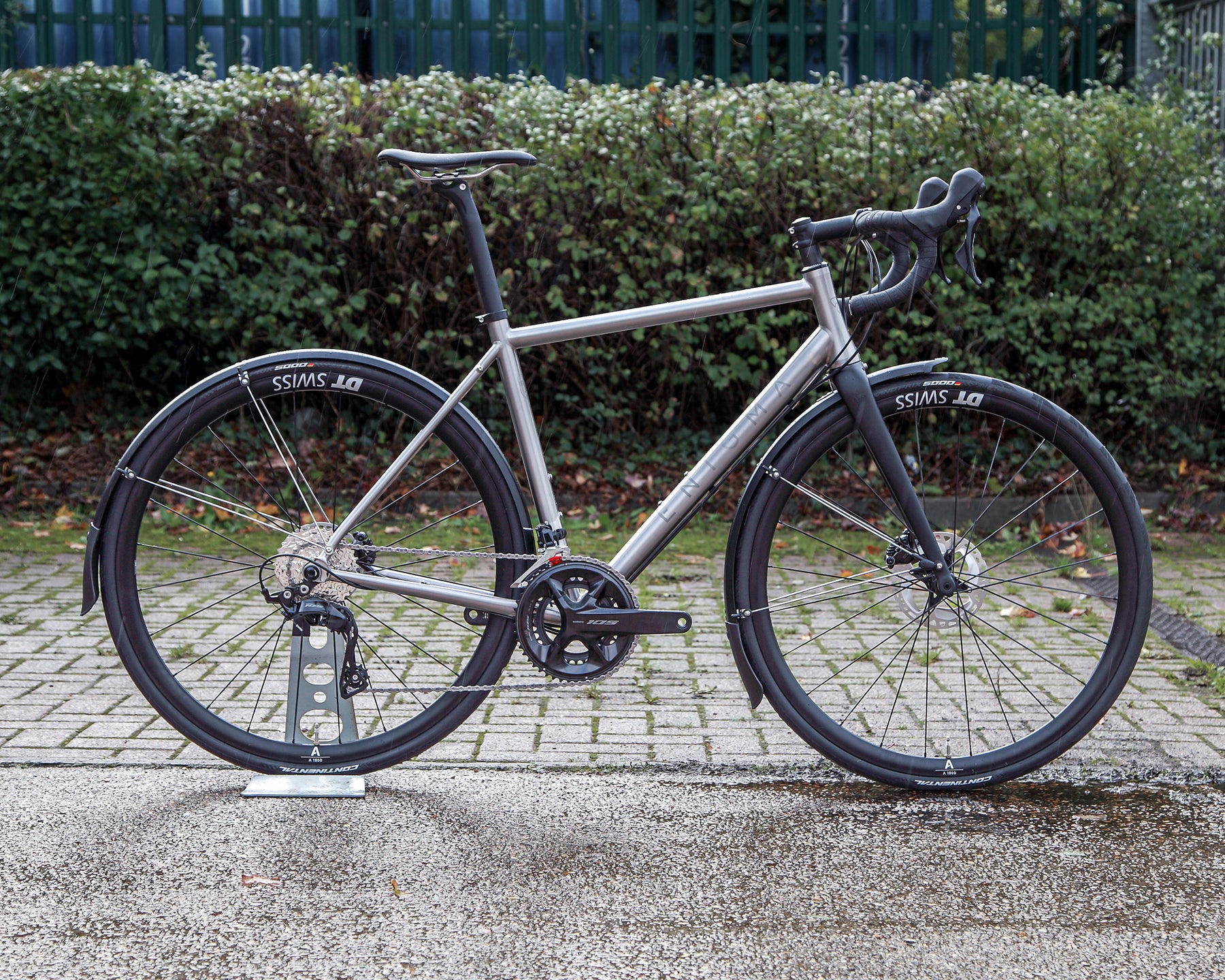 Enigma Etape 54cm titanium all-road bike, side-on view featuring brushed titanium frame, Shimano 105 drivetrain, DT Swiss wheels, carbon fork and mudguards.